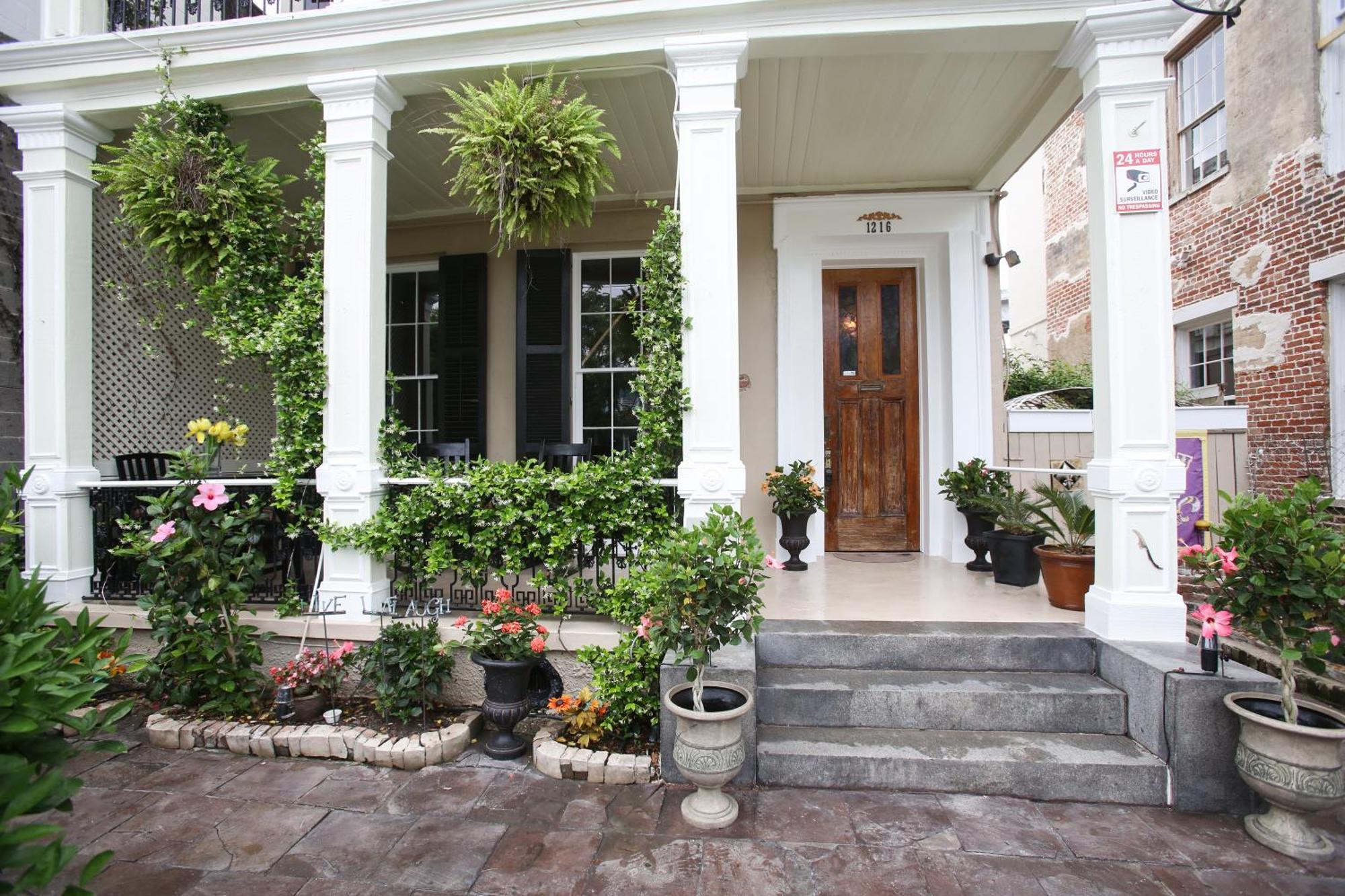 A house with a white porch and columns, surrounded by plants and flowers.